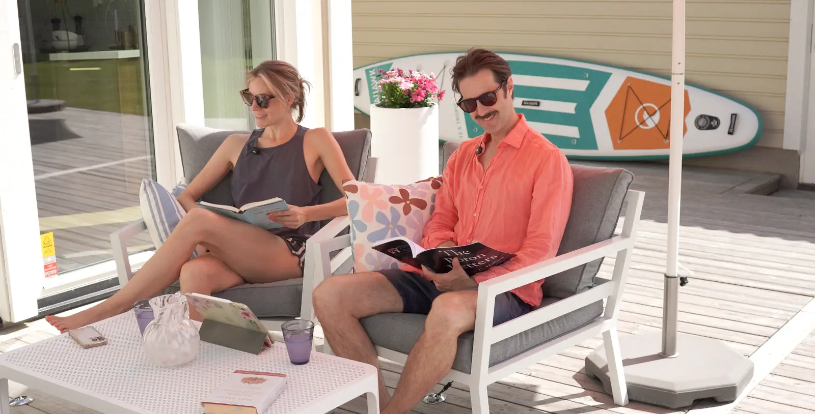 Erika and Martin reading in the sun on the terrace, a paddleboard leaning behind them